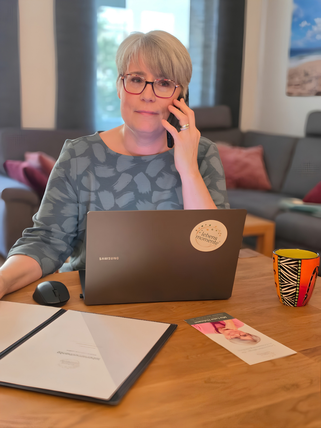 Mia Luise Hofmann telefoniert mit dem Handy, vor ihr stehen ein Laptop und Unterlagen auf dem Tisch